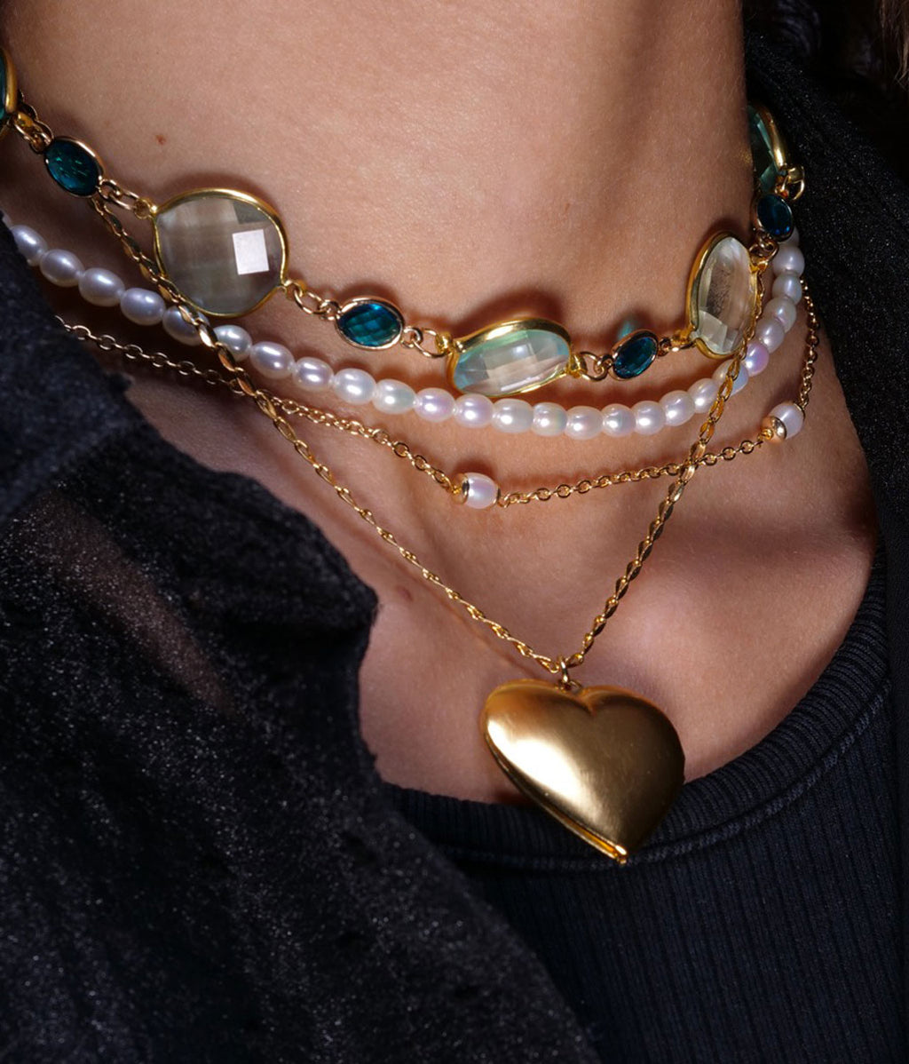 Collier cœur doré portée avec un collier bleu et un collier de perle sur femme